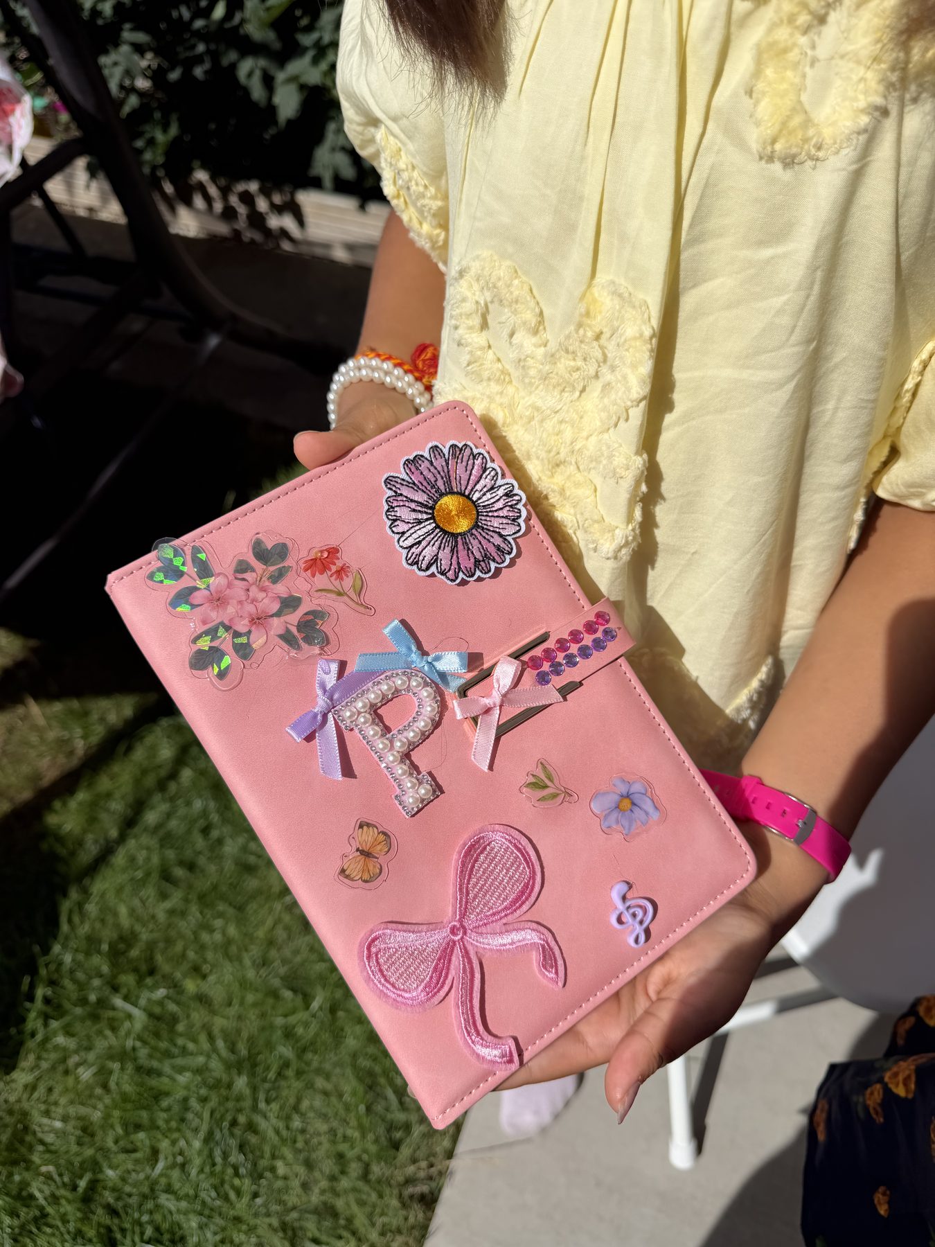 Child holding a pink journal decorated with flower patches and a bow at a craft party