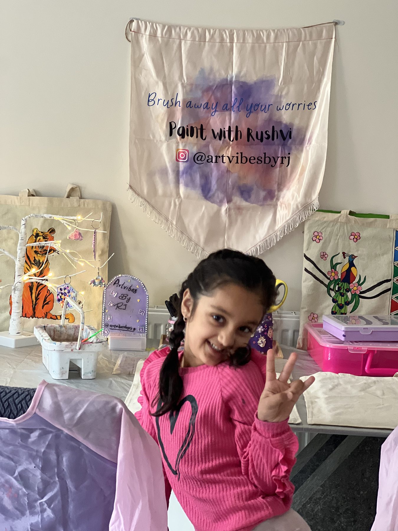 A girl at an Artvibes By RJ children's craft party, decorating tote bags in front of the studio banner
